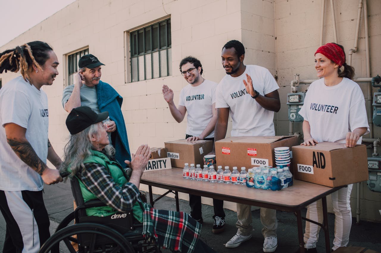 hero-contact Group of volunteers providing food and aid to a person in wheelchair outdoors.